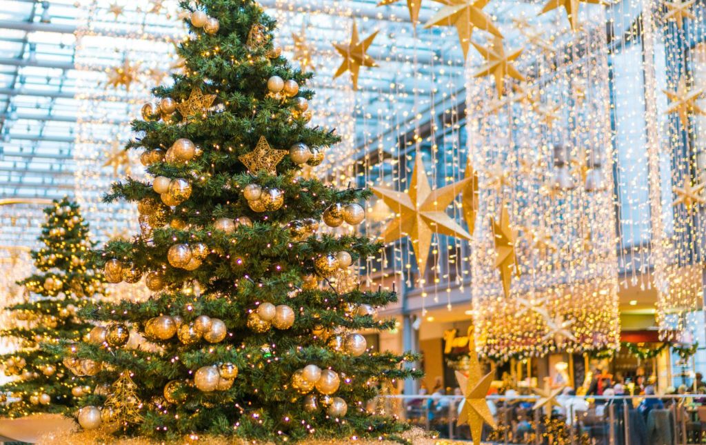 Christmas holiday decorations in a commercial shopping mall with two gold themed evergreen Xmas trees and golden stars suspended from the ceiling